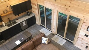 Ein modernes Interieur einer Blockhütte mit Küche, Essbereich und einer großen Schiebeglastür, die auf eine Terrasse führt.