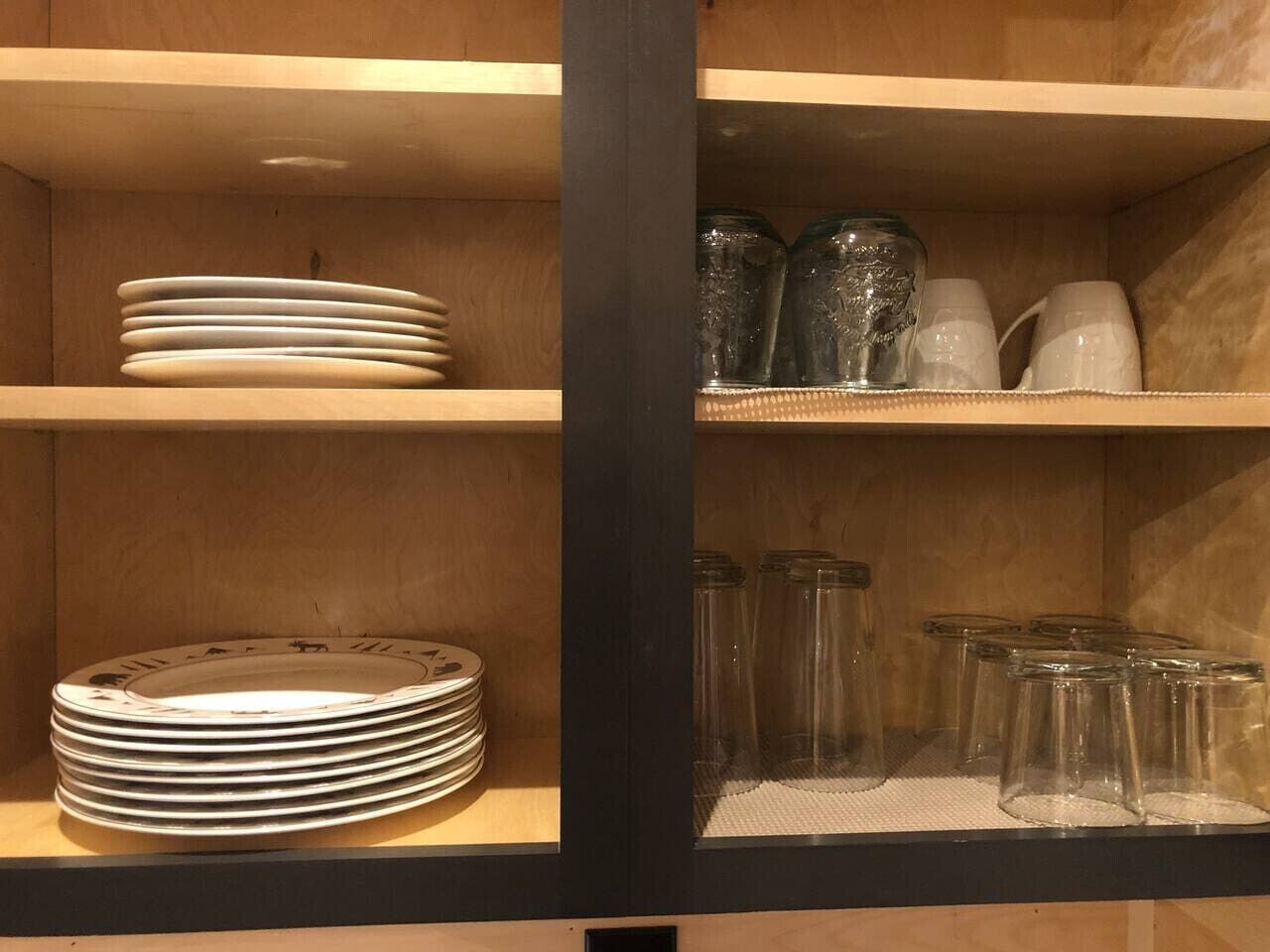 A wooden shelf with stacked plates and clear glass jars.