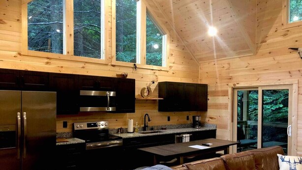 Ein modernes Blockhaus-Interieur mit Küche, Essbereich und großem Fenster mit Blick auf einen Wald.