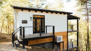 Een klein houten huisje, genaamd 'White Pine', met een houten terras, een trap en een airconditioning.