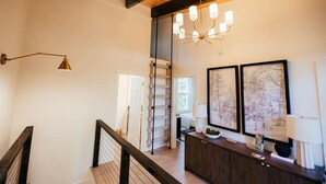 Een trap met houten leuning, een kroonluchter en uitzicht op een kamer met een bureau en ingekaderde foto's.