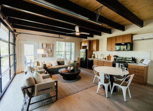 A spacious living area with a sofa set, a coffee table, and a dining table with chairs. There is a kitchen area with cabinets and appliances.