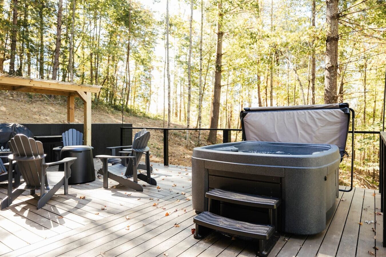 A deck with a hot tub, Adirondack chairs, and a grill.
