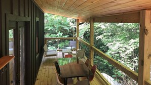 A wooden deck with a table and chairs, overlooking a lush green forest.