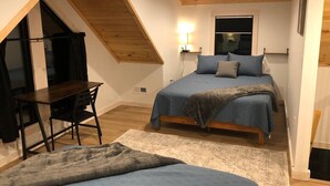 A bedroom with a sloped ceiling, a bed with blue bedding, a desk with a chair, and a window.
