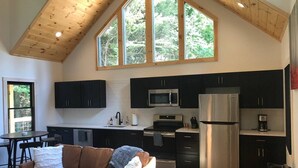 A modern kitchen with dark cabinets, stainless steel appliances, and a large window.