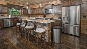 A spacious kitchen with wooden cabinetry, a central island with stools, stainless steel appliances, and a large window providing natural light.