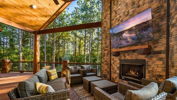 A covered outdoor seating area with wicker furniture, a fireplace, and a large landscape painting on the wall.