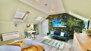 A modern bedroom with a large bed, a green sofa, a TV, and a wall with a tropical mural.