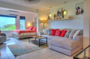 A modern living room with a sofa, a coffee table, and a bed with a colorful bedspread. - Ocean Views, Pool & Space for Groups (Vieques)