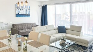 Een moderne woonkamer met een hoekbank, een glazen salontafel en een eethoek met een glazen tafel en stoelen.