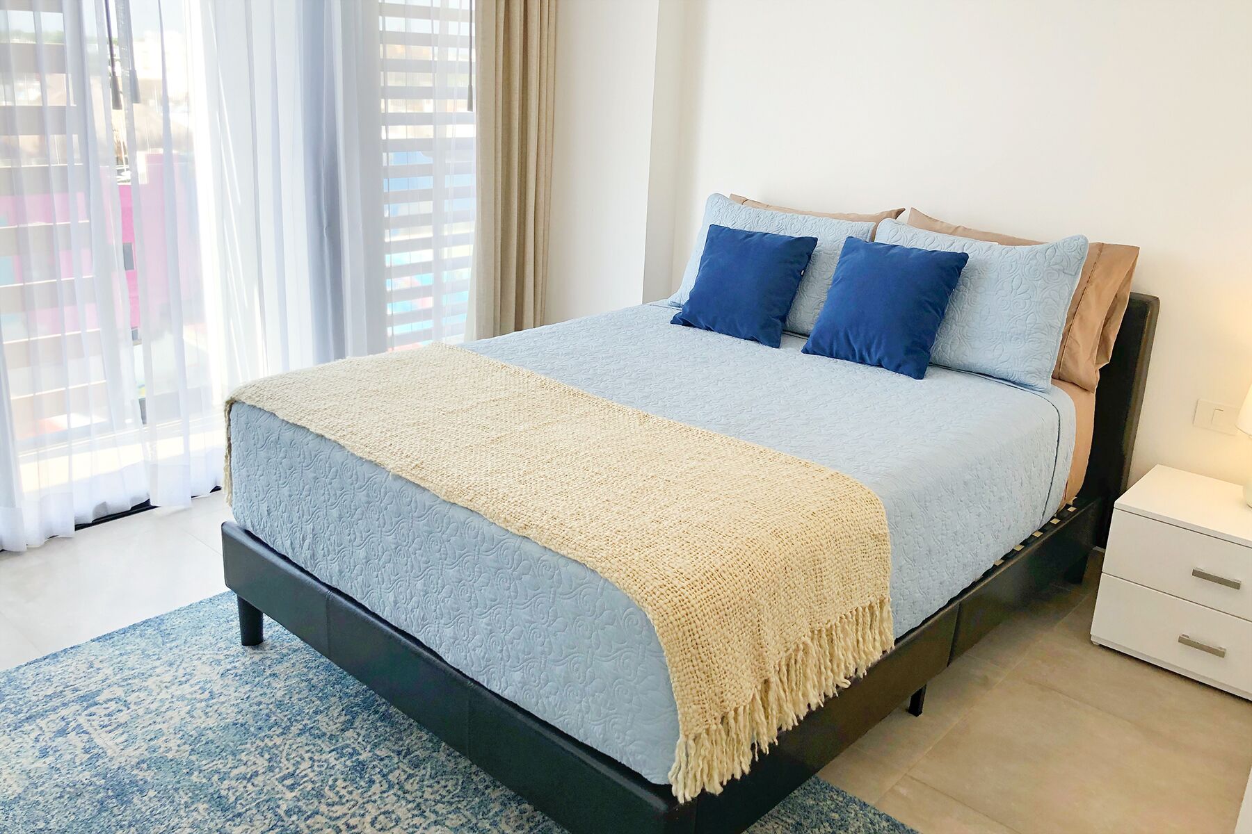 A neatly made bed with a blue and beige bedspread, two blue pillows, and a beige throw blanket.