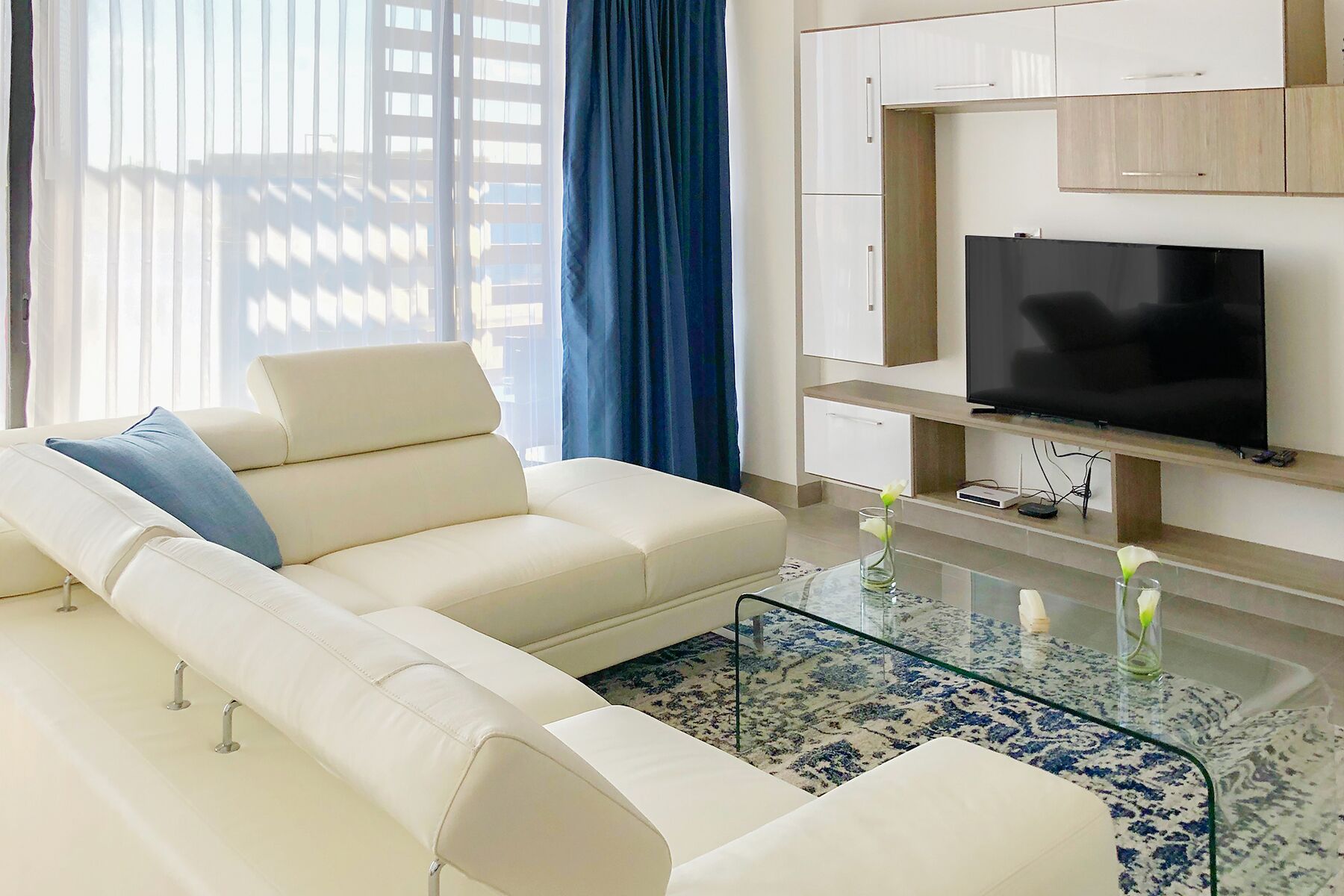 Ein modernes Wohnzimmer mit einem weißen Sofa, einem Glastisch und einem Flachbildfernseher.