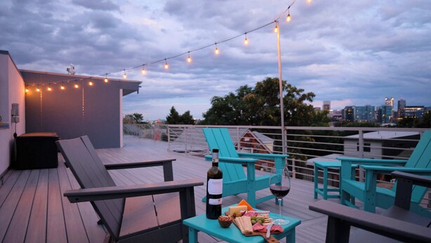 En tagterrasse med udendørs siddepladser, lyskæder og en vinflaske.