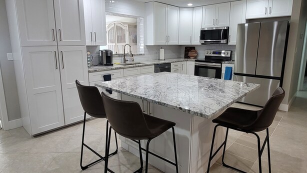 A modern kitchen with white cabinets, a marble island, and stainless steel appliances. - Waterfront gulf access retreat in coveted SW cape. Bring your boat!  (Cape Coral)