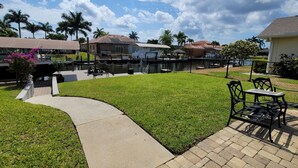 A well-maintained outdoor area with a paved walkway, a grassy lawn, and a seating area with tables and chairs. - Waterfront gulf access retreat in coveted SW cape. Bring your boat!  (Cape Coral)