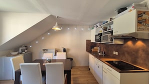 Eine moderne Küche mit Essbereich, ausgestattet mit einem Holztisch, weißen Stühlen, einem Einbauofen und einer Mikrowelle.