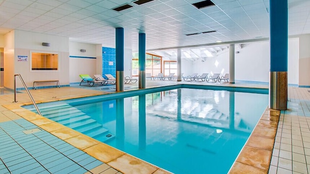Ein beheiztes Hallenbecken mit klarem Wasser, gefliestem Boden und Liegestühlen.