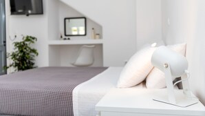 Moderni makuuhuone, jossa on sänky, yöpöytä lampun kanssa, työpöytä tietokonenäytöllä ja seinälle asennettu televisio.