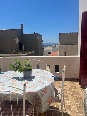 A rooftop terrace with a table and chairs, a potted plant, and a view of buildings and mountains. - Makares Downtown Apartments (Naxos)