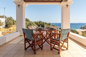 Un espacio comedor al aire libre techado con una mesa y sillas, con vista a un paisaje costero.