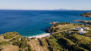 Vista aérea de una zona costera con playa, terreno rocoso y edificios blancos de techos planos.
