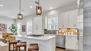 A modern kitchen with white cabinets, a large island, bar stools, and pendant lighting. - Guest Favorite Beach Beauty with Bunks SLPS 8! (Inlet Beach)