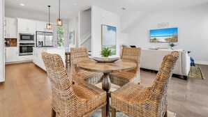 A modern kitchen with white cabinets, stainless steel appliances, and a dining area with wicker chairs and a round table. - Guest Favorite Beach Beauty with Bunks SLPS 8! (Inlet Beach)