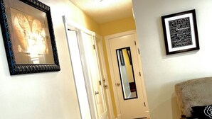A hallway with a framed picture on the left, a mirror on the right, and a door at the end.