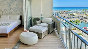 A balcony with a bed, a round table with drinks, and a view of a marina and beach.