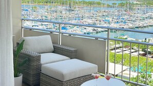 A balcony with a view of a marina, wicker furniture, a potted plant, and a round table with a drink.