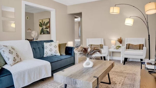 Una sala de estar moderna con un sofá azul, sillones blancos, una mesa de centro de madera y una lámpara de pie.