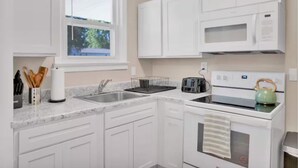 Una cocina moderna con armarios blancos, un microondas integrado, un tostador y una tetera sobre la estufa.