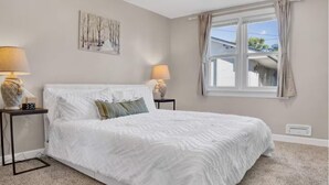 Un dormitorio con una cama grande, dos mesitas de noche con lámparas, un cuadro en la pared y una ventana con cortinas.