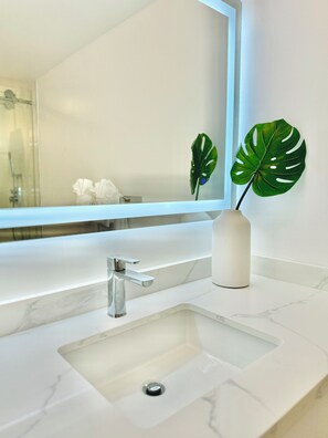 A bathroom with a white sink, a mirror, and a potted monstera plant. - Oceanfront Dream Home (Car Available) (Honolulu)