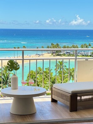 A balcony with a view of the ocean, a table with drinks, and a lounge chair. - Oceanfront Dream Home (Car Available) (Honolulu)