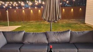 A cozy outdoor seating area with a sofa and a table, a bottle of wine, and two glasses.