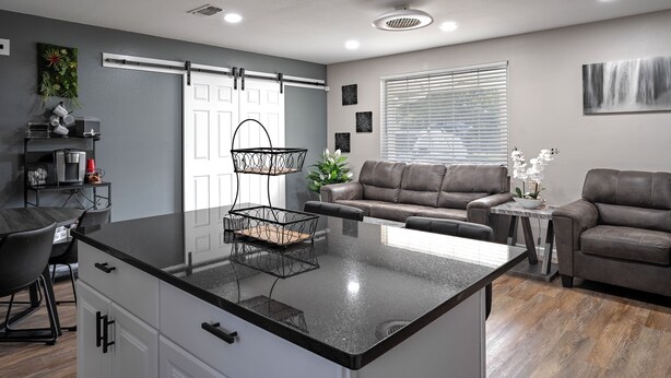 A modern kitchen with a central island, a dining area with a table and chairs, a sofa, and a window with blinds.