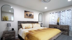 A bedroom with a large bed, wooden headboard, two bedside tables with lamps, a mirror, and a framed picture on the wall.