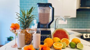 A kitchen counter with a blender, fresh fruits, and flower arrangements. - Oceanfront Paradise (Car Available) (Honolulu)