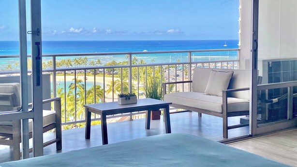 A balcony with a view of the ocean, a sofa, a table, and a potted plant.