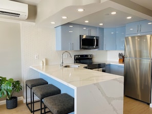 A modern kitchen with a central island, stainless steel appliances, and blue cabinets. - Oceanfront Sunset Home (Car Available) (Honolulu)