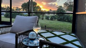A wicker chair with a cushion and a glass table with a wine glass and a decorative item. - Paradise awaits! Heated pool, huge lanai, outdoor oasis close to downtown Naples (Naples)