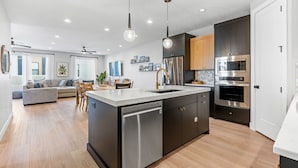 A modern kitchen with a central island, stainless steel appliances, and a dining area with a sofa and chairs. - Hukilau House - St. George 5 Bedroom Townhouse (St. George)
