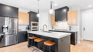 A modern kitchen with a large island, stainless steel appliances, wooden bar stools, and pendant lighting. - Hukilau House - St. George 5 Bedroom Townhouse (St. George)