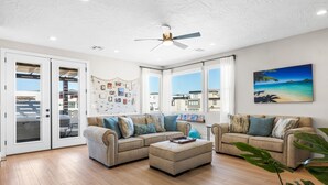 A spacious living room with a beige sofa set, a coffee table, and a ceiling fan. - Hukilau House - St. George 5 Bedroom Townhouse (St. George)