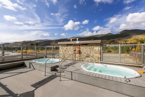 Relax on the rooftop terrace with panoramic views of the surrounding mountains, featuring two hot tubs and a wooden deck.