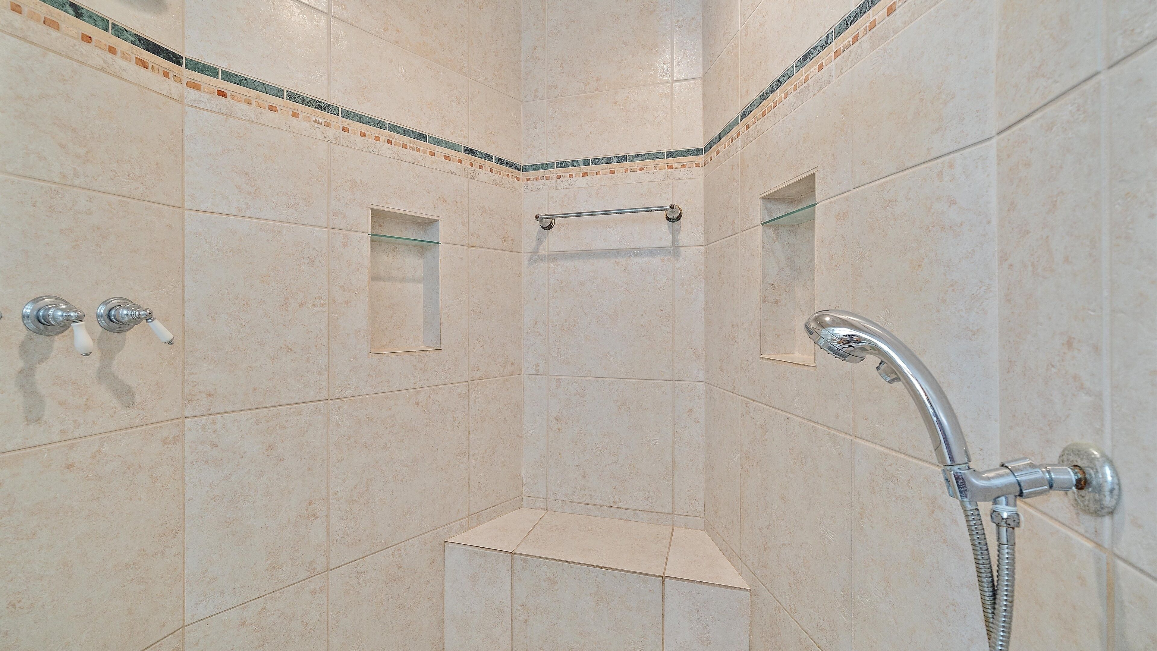 A corner shower with beige tiles, a glass shelf, and a handheld showerhead.