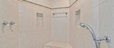 A corner shower with beige tiles, a glass shelf, and a handheld showerhead.