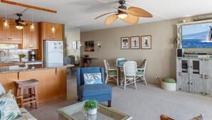 A modern living room with a kitchen area, featuring a dining set, a sofa, a coffee table, and a ceiling fan. - Kihei Ali'i Kai D202 1 Bedroom Condo (Kihei)